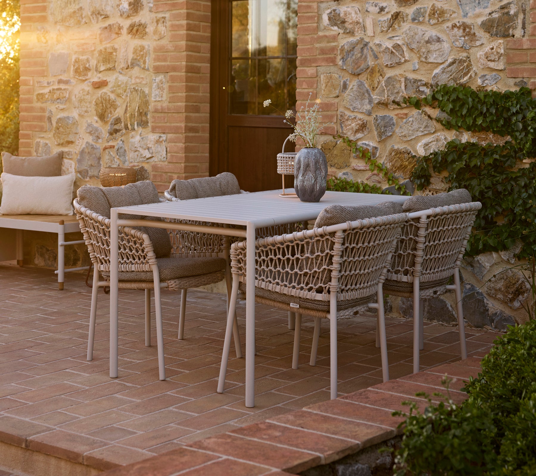 Beachy dining setup featuring a Bliss table surrounded by Ocean dining chairs, set against a charming stone backdrop.