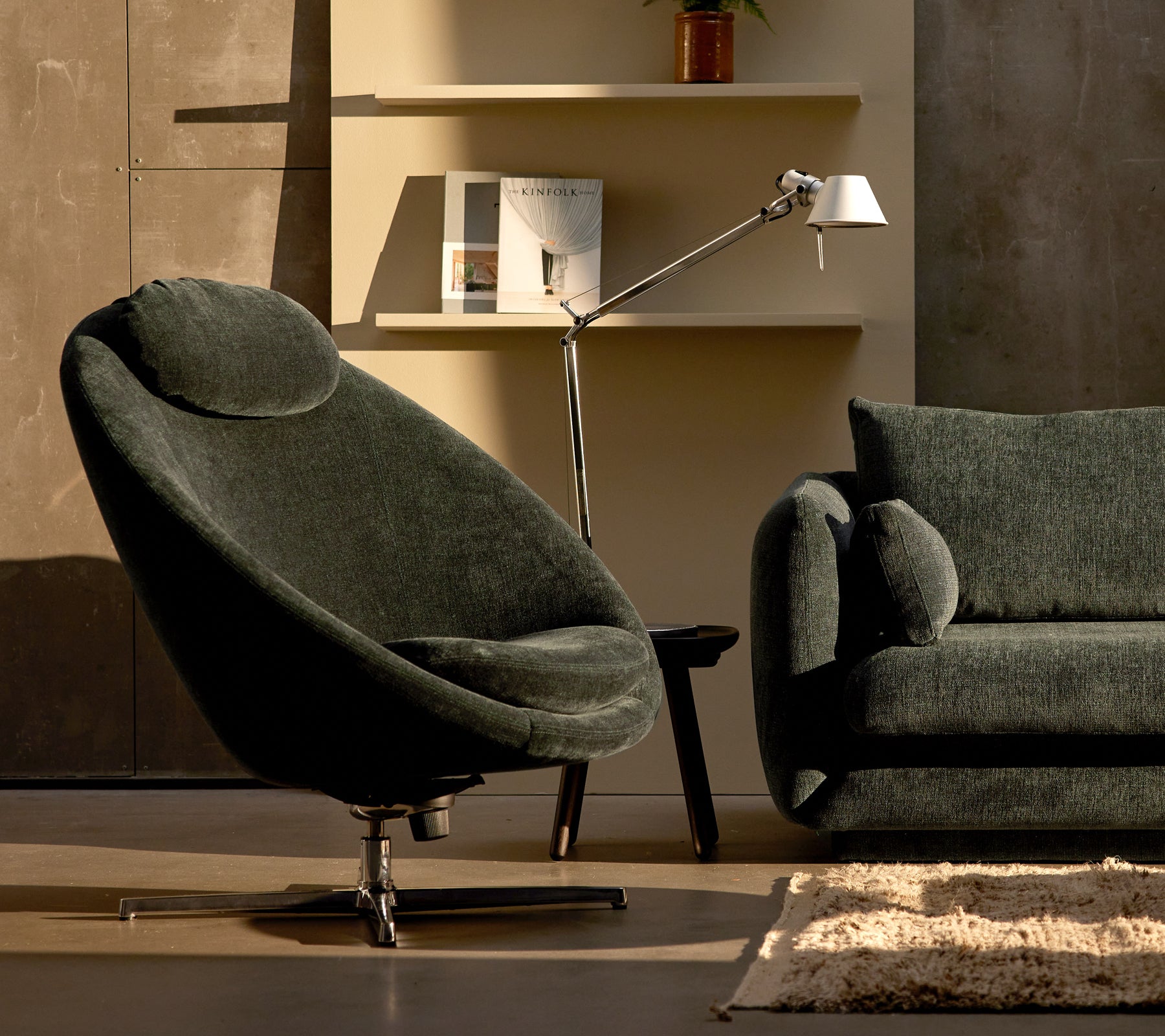 Pace chair in dark green chenille next to a Bloom sofa, complemented by a sleek lamp and minimalistic shelf decor.