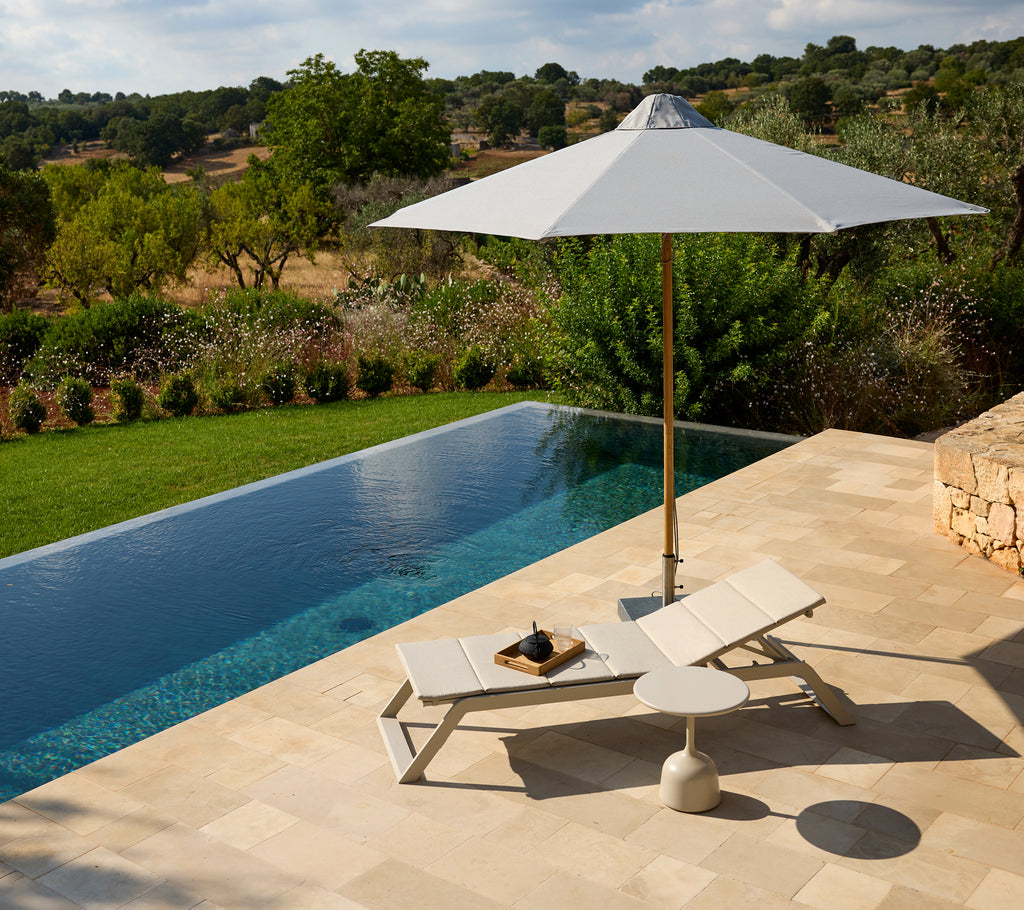 Modern outdoor lounge area featuring a white chair, umbrella, and side table by a pool.