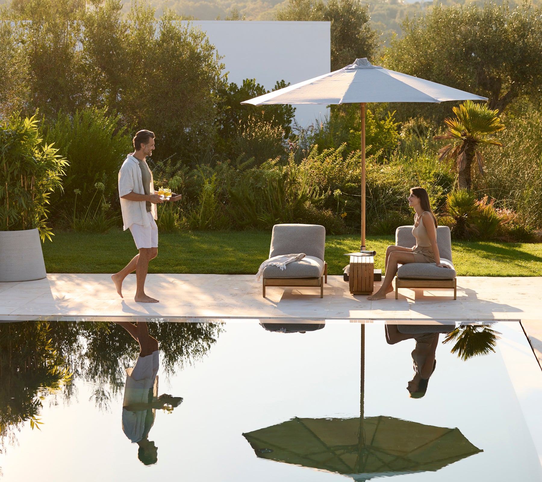 Outdoor modern lounge area featuring grey chairs, a wooden table, and a green umbrella.