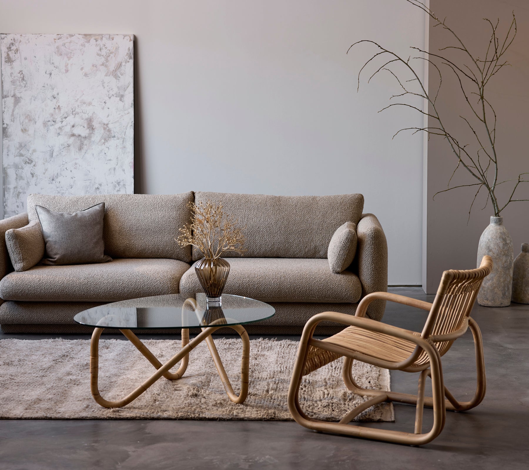 Contemporary lounge setup featuring a beige sofa, glass table, and woven chair.